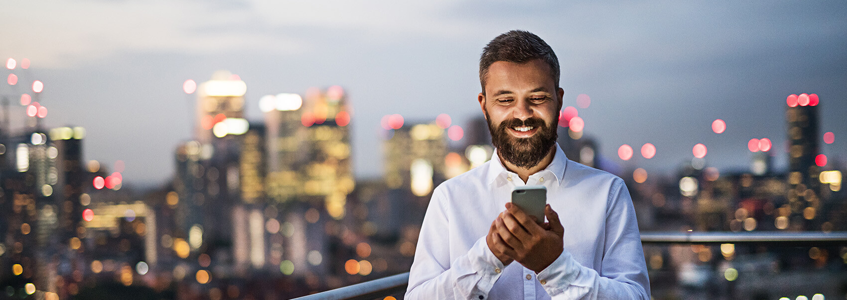 man with beard smiling at his phone with a city scape in the background