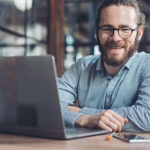Man with Beard Smiling with laptop on desk in front of him