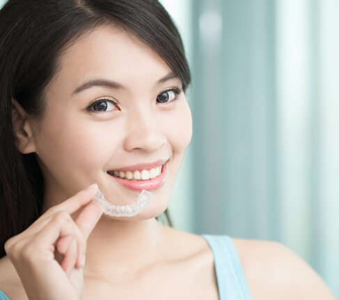 young woman holding up a set of clear aligners