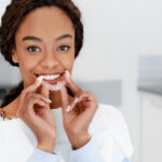 Black woman smiles while putting in her Invisalign clear aligner