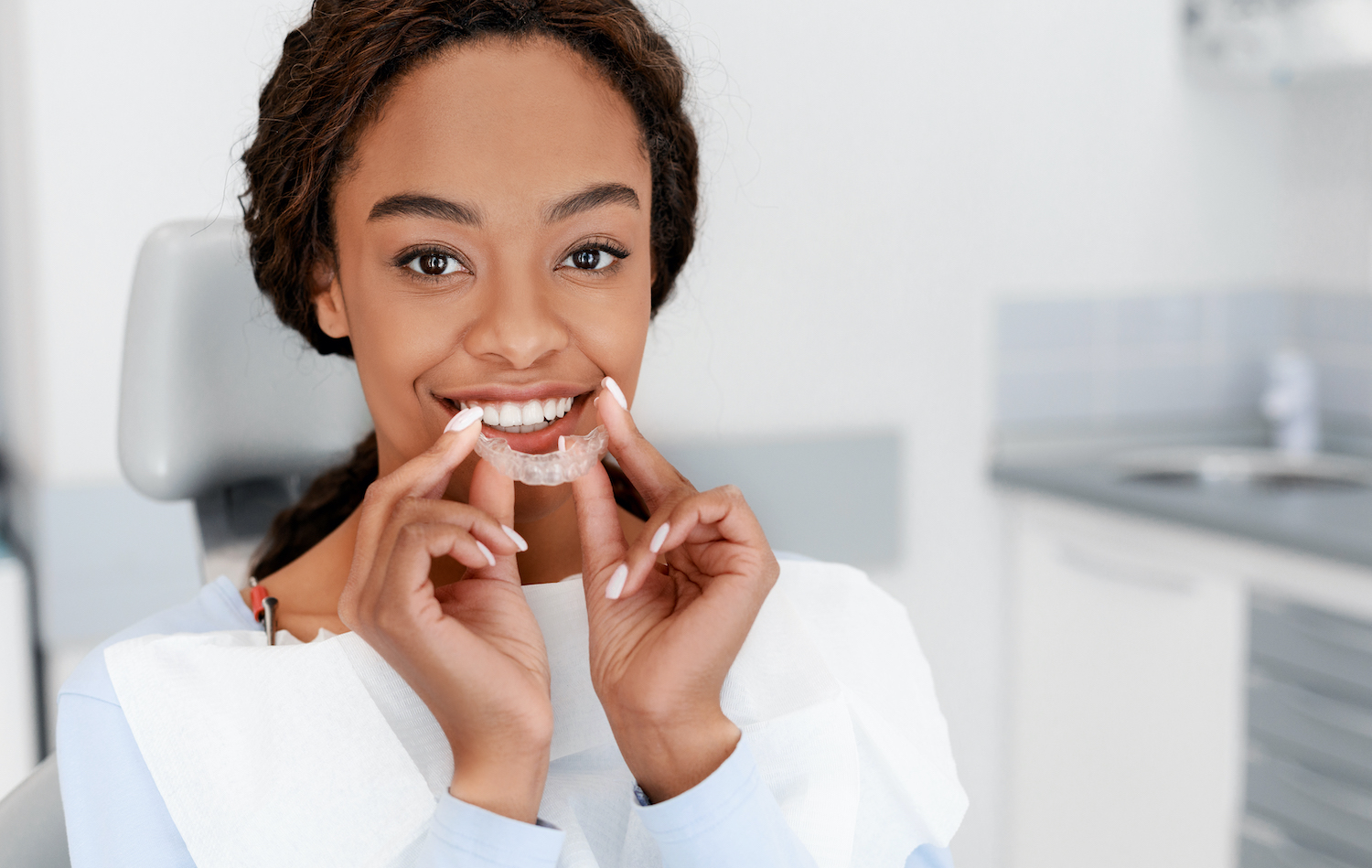 Black woman smiles while putting in her Invisalign clear aligner