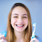 Photograph of young woman with braces holding a toothbrush and floss. Life with braces includes brushing and flossing your braces.