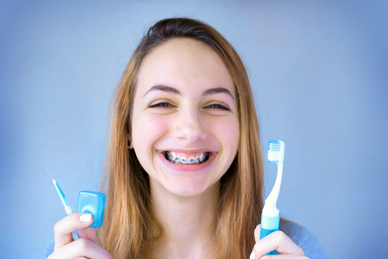 Photograph of young woman with braces holding a toothbrush and floss. Life with braces includes brushing and flossing your braces.