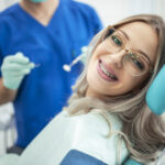 common questions about braces, woman with braces smiling in dental chair, wearing glasses