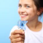 young girl holding her retainer although it can be hard to get kids to wear their retainer
