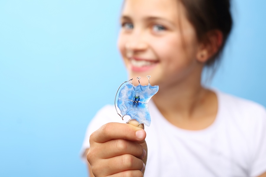 young girl holding her retainer although it can be hard to get kids to wear their retainer